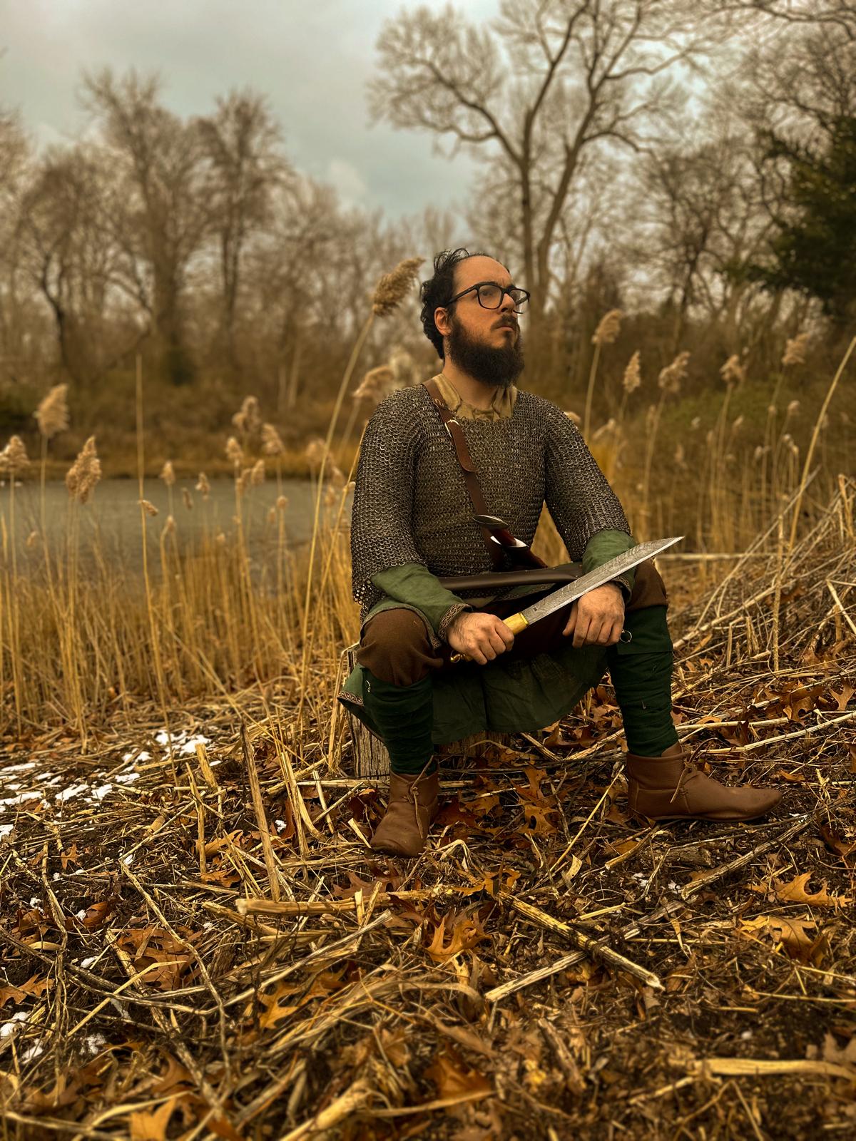 A Viking warrior in a dreary background sitting on a tree stump, holding a seax